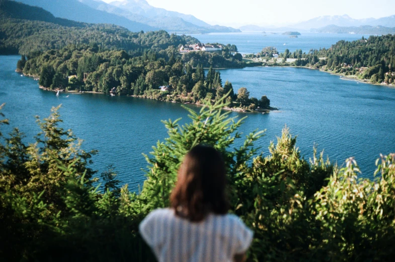 a woman standing on top of a lush green hillside, by Sophie Pemberton, pexels contest winner, lake house, chile, half turned around, against the backdrop of trees