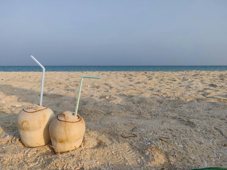 two coconut drinks sitting on top of a sandy beach, unsplash, minimalism, tanned ameera al taweel, middle east, multiple stories, exterior shot