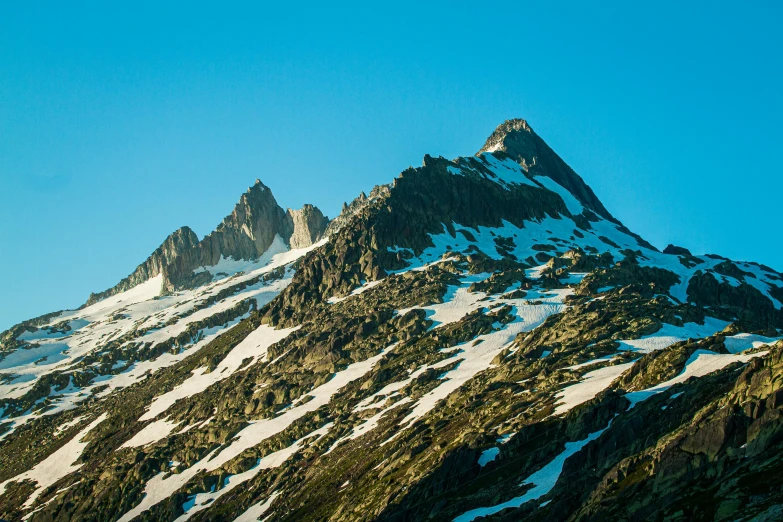 the top of a mountain covered in snow, by Werner Andermatt, unsplash contest winner, asymmetrical spires, seen from a distance, pacific northwest, clear blue skies