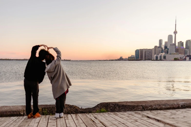 a couple of people standing next to a body of water, pexels contest winner, toronto city, loving embrace, spring evening, contorted