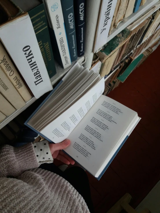 a person holding a book in front of a bunch of books, by Penelope Beaton, reddit, low quality photo, swedish writing, high angle close up shot, on a pedestal