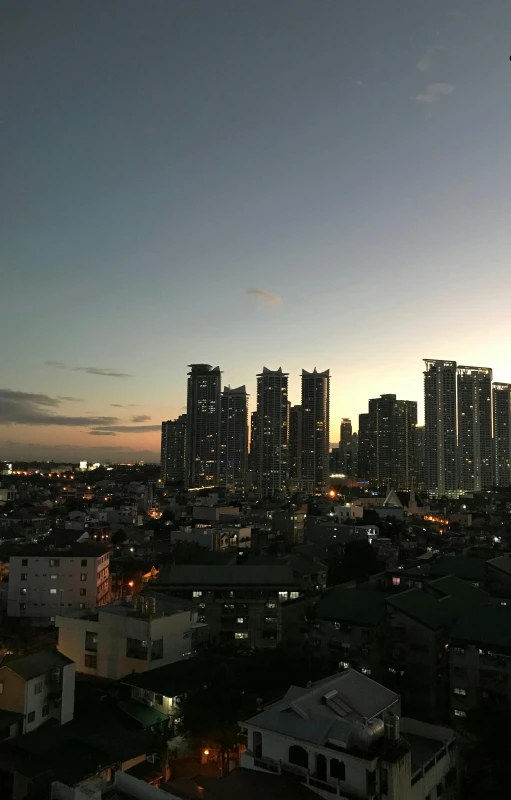 an airplane flying over a city at dusk, a picture, happening, manila, skyline view from a rooftop, front facing, with towers