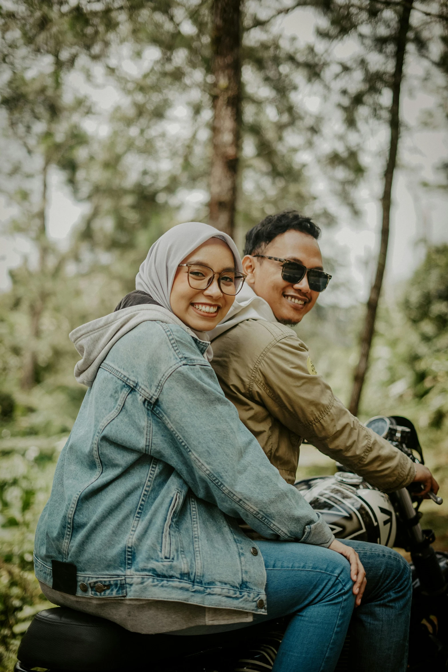 a man and woman riding on the back of a motorcycle, pexels contest winner, sumatraism, wearing small round glasses, sitting in the forrest, flirting smiling, islamic