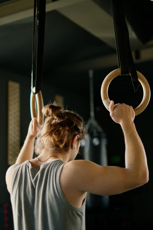 a woman hanging on rings in a gym, trending on pexels, square, small details, on black background, manuka