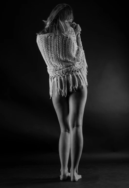 a woman standing in the dark with her back to the camera, a black and white photo, inspired by irakli nadar, cgsociety, arabesque, wearing sweater, legs stretched!!! intricate, stringy, lowres