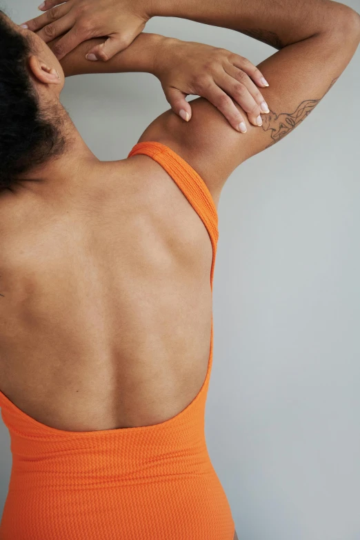 a woman in an orange one piece swimsuit, a tattoo, inspired by Michaelangelo, trending on pexels, showing her shoulder from back, depressed dramatic bicep pose, detailed product shot, viridescent at shoulder height