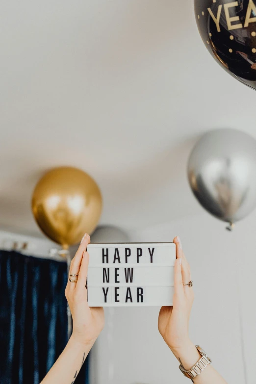 a woman holding up a sign that says happy new year, trending on unsplash, balloon, multiple stories, grey, holding flask in hand