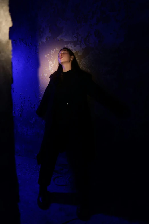 a woman that is standing in the dark, ambient cave lighting, wearing long black winter coat, ( ( theatrical ) ), dramatic blue lighting