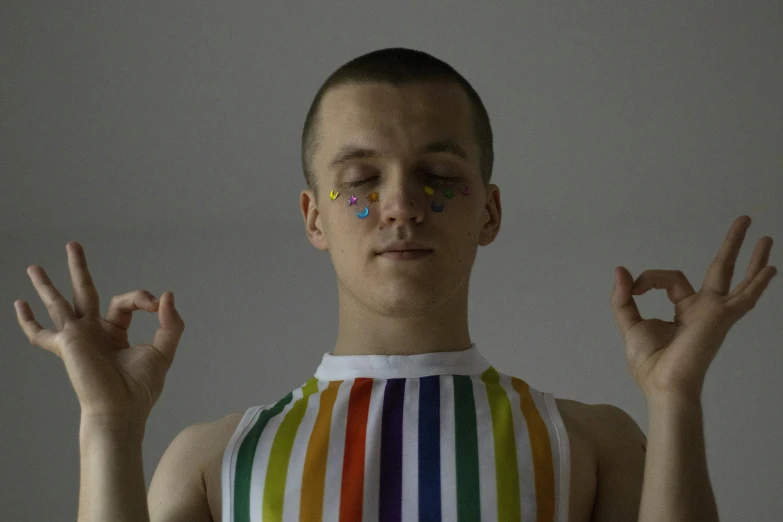 a man making a peace sign with his hands, by Attila Meszlenyi, aestheticism, rainbow clothes, padmasana, genderless, vitalik buterin