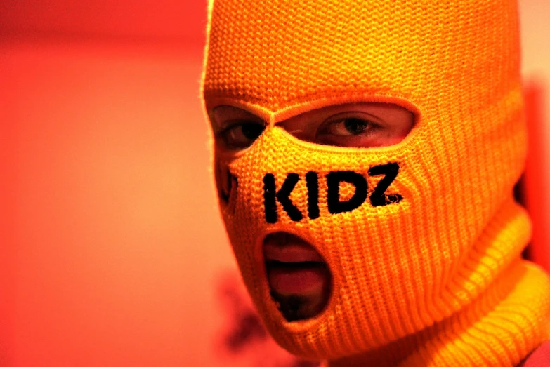 a person wearing a ski mask with the word kidz written on it, an album cover, mustard, ap photo, krzysztof kononowicz, kid a