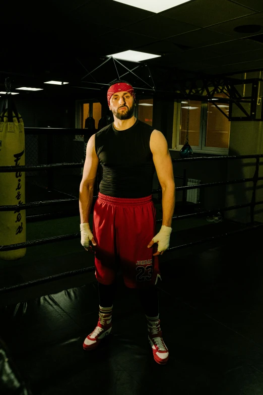 a man standing in the middle of a boxing ring, inspired by Volkan Baga, wearing a red backwards cap, aaron rodgers, looking straight to camera, standing in a dimly lit room