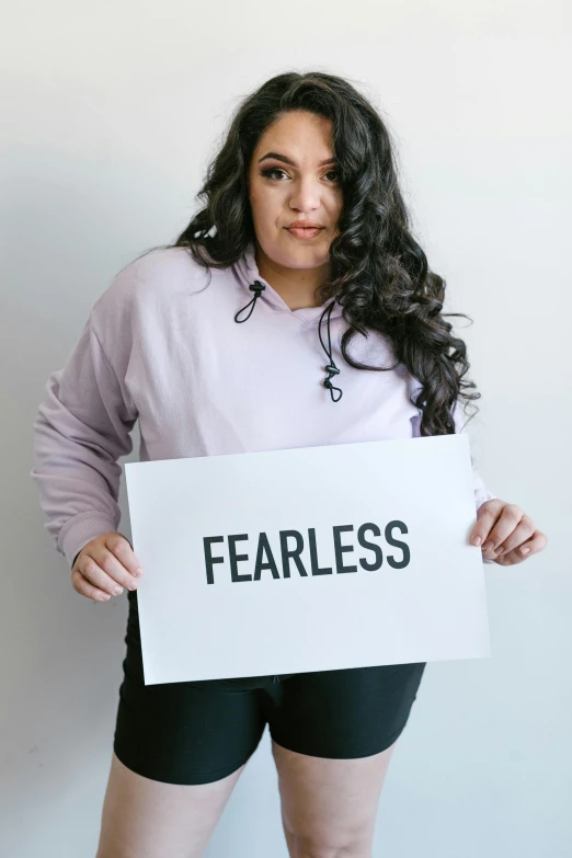 a woman holding a sign that says fearless, by Arabella Rankin, trending on pexels, plus size, ((purple)), seamless, sweat