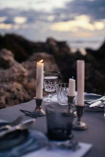 a couple of candles sitting on top of a table, on the ocean, place setting, with jagged rocks & eerie, eating outside