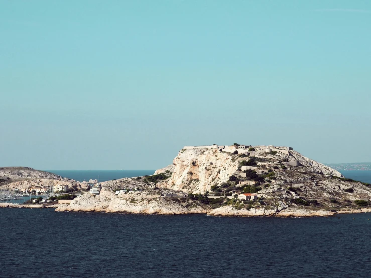 a small island in the middle of a large body of water, inspired by Wilhelm Marstrand, unsplash, romanticism, over a calanque, whitewashed housed, in the distance is a rocky hill, conde nast traveler photo