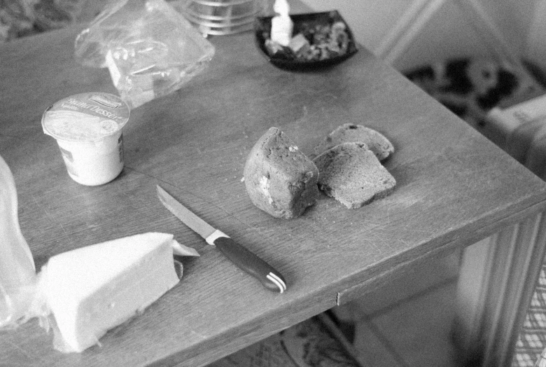 a piece of bread sitting on top of a table next to a knife, a still life, by Maurycy Gottlieb, fluxus, cheeses, tri - x, unknown artist, messy