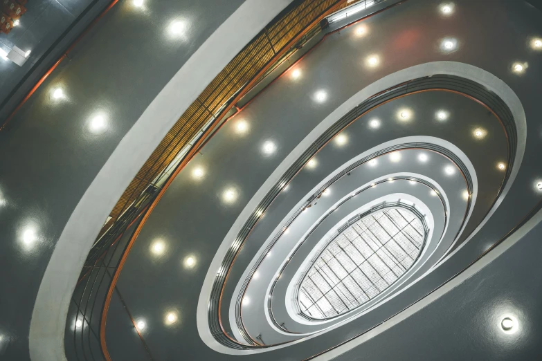 a spiral staircase in a building with lots of lights, inspired by Alexander Rodchenko, unsplash contest winner, bauhaus, recessed, large hall, high school, zezhou chen