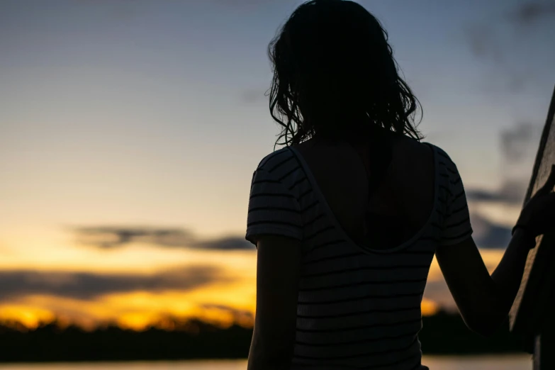 a woman standing next to a body of water, in the sunset, teenage girl, subtle detailing, self deprecating