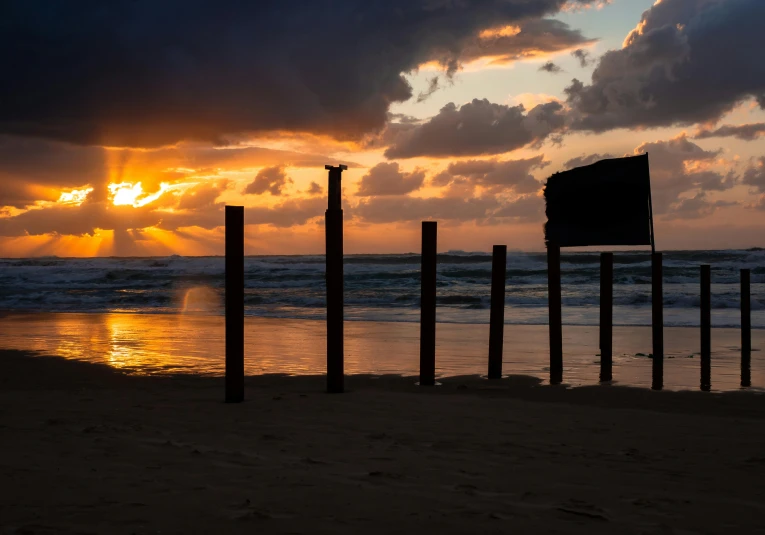 a sign sitting on top of a sandy beach next to the ocean, pexels contest winner, australian tonalism, sunset lighting 8k, wooden structures, profile image, stanchions