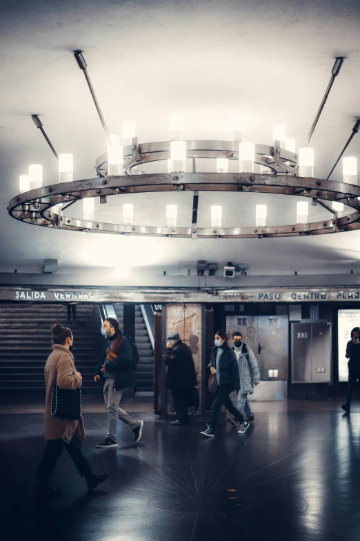 a group of people walking through a subway station, by Adam Marczyński, trending on unsplash, art nouveau, light fixtures, circular, big chandelier, inside a brutalist space ship