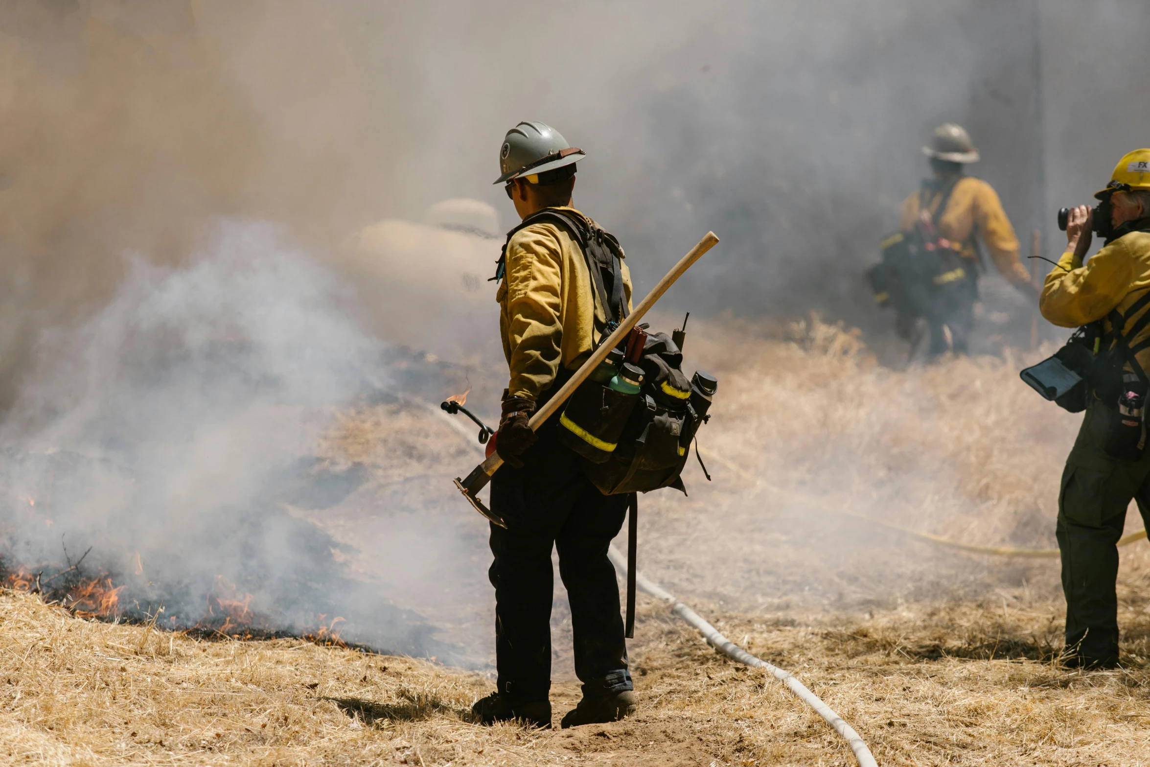 a group of firefighters standing on top of a grass covered hillside, pexels contest winner, figuration libre, heat haze, a wooden, person in foreground, bay area