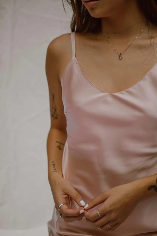 a woman in a pink dress holding a cell phone, a tattoo, inspired by Elsa Bleda, trending on pexels, renaissance, wearing white camisole, closeup - view, soft silk dress, bralette