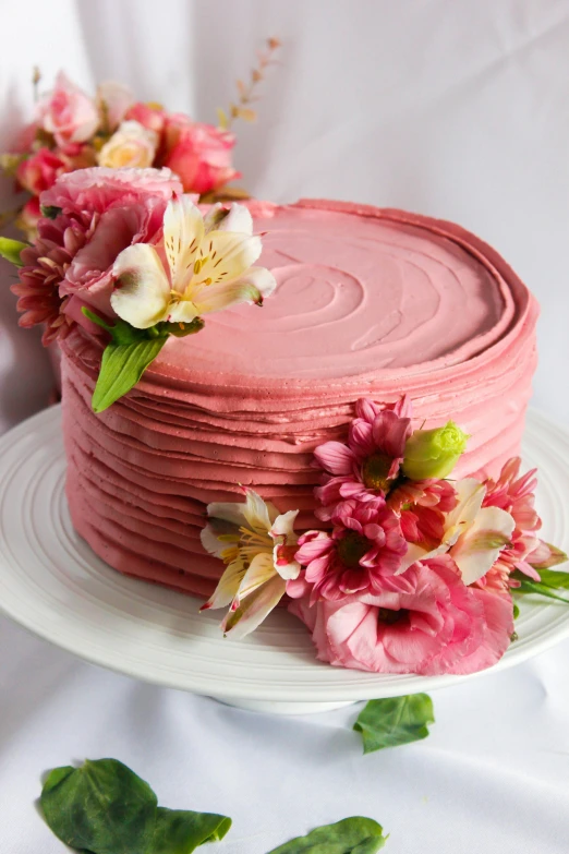 a pink cake sitting on top of a white plate, full of flowers