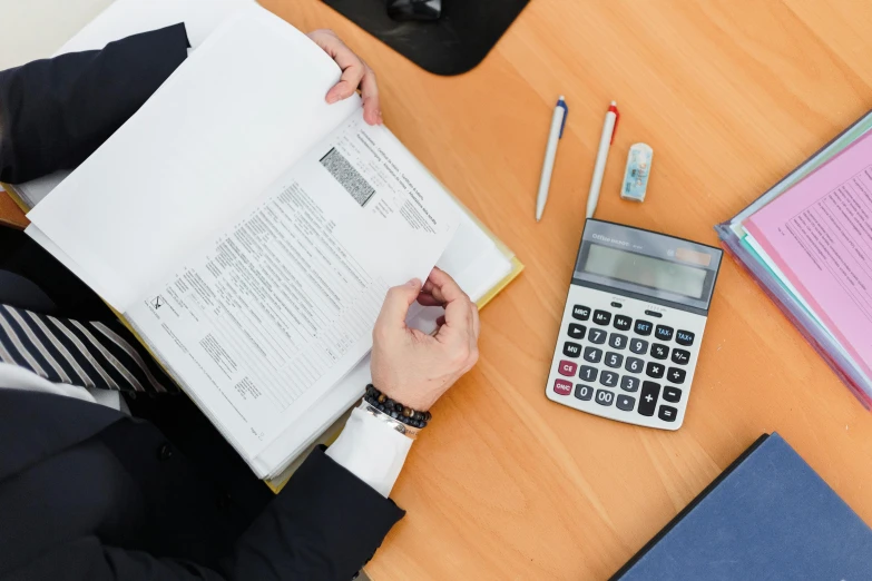 a person sitting at a table with a book and a calculator, on a desk