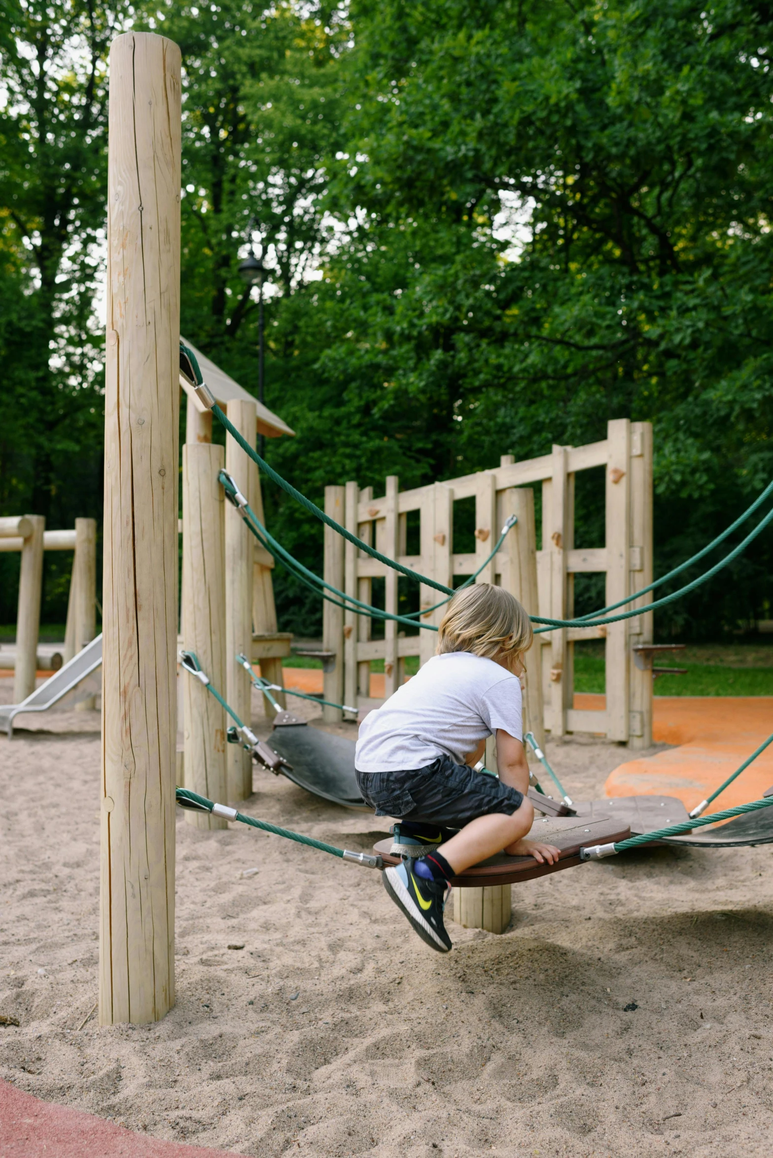 a young boy playing in the sand at a playground, by karlkka, rope bridges, berlin park, soft surfaces, wooden banks