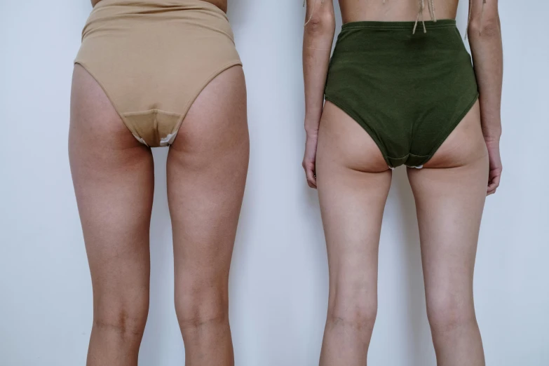 a couple of women standing next to each other, a colorized photo, unsplash, thigh gap, olive thigh skin, toned derriere, anthro