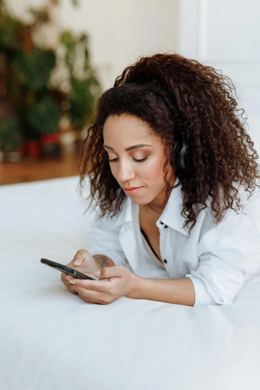 a woman laying on a bed using a cell phone, trending on pexels, curls, wearing a white button up shirt, mixed-race woman, ad image