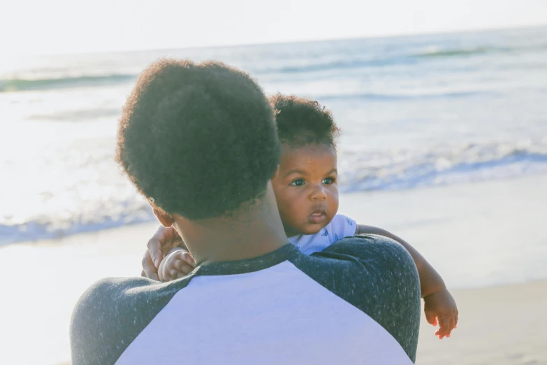 a man holding a baby on the beach, pexels contest winner, brown skinned, 1 2 9 7, blank, varying ethnicities