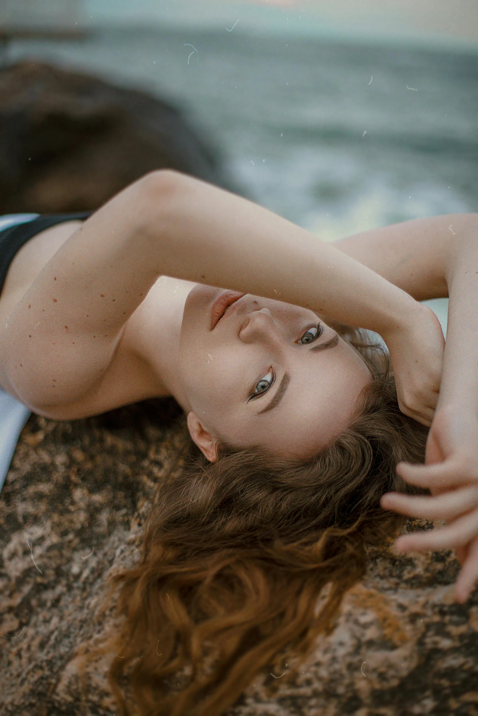 a woman laying on top of a rock near the ocean, inspired by Elsa Bleda, trending on pexels, renaissance, androgynous face, light cute freckles, contorted, wavy hair spread out