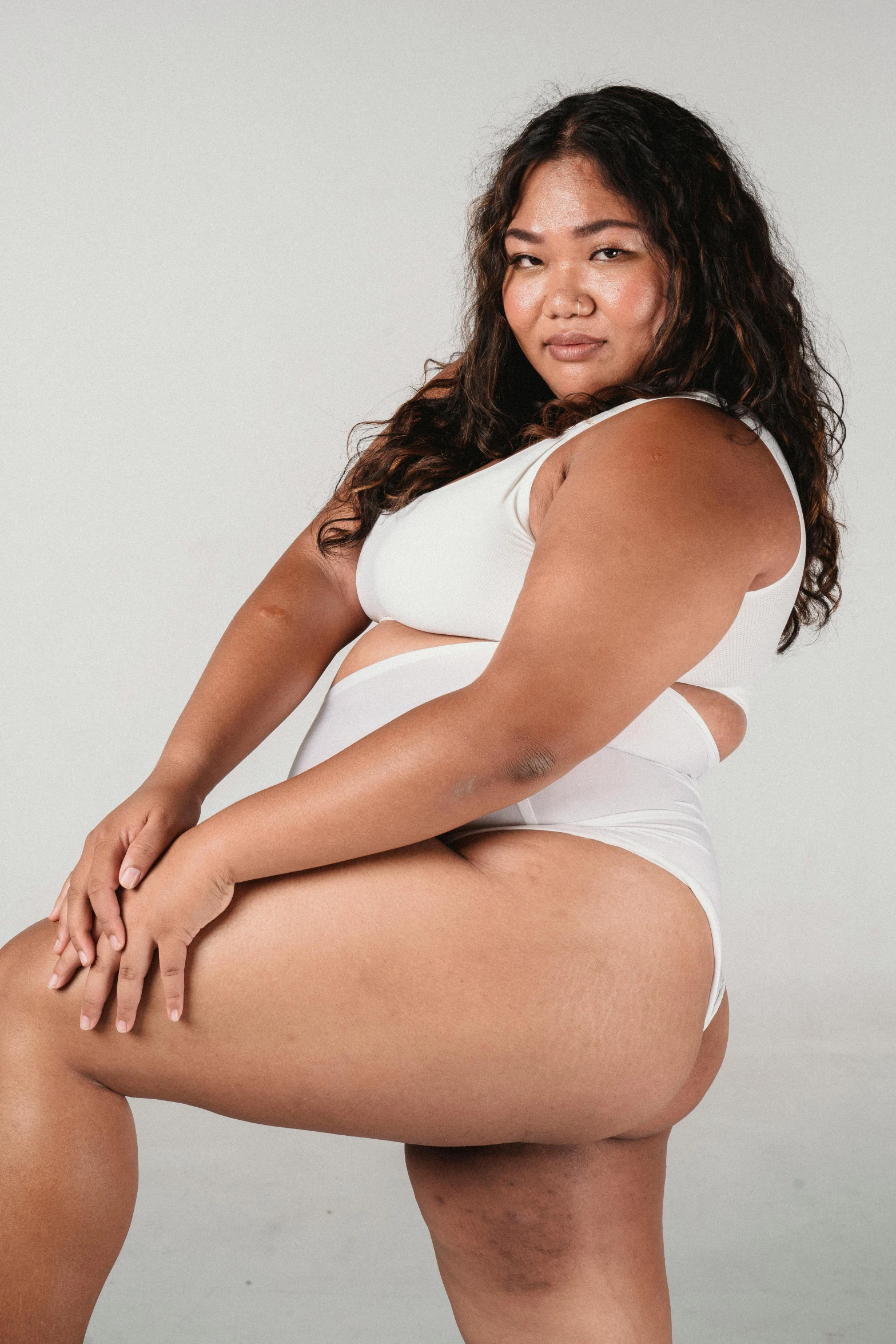 a woman in a white bikini posing for a picture, an album cover, unsplash, bbwchan, plain background, sitting down casually, underwear ad