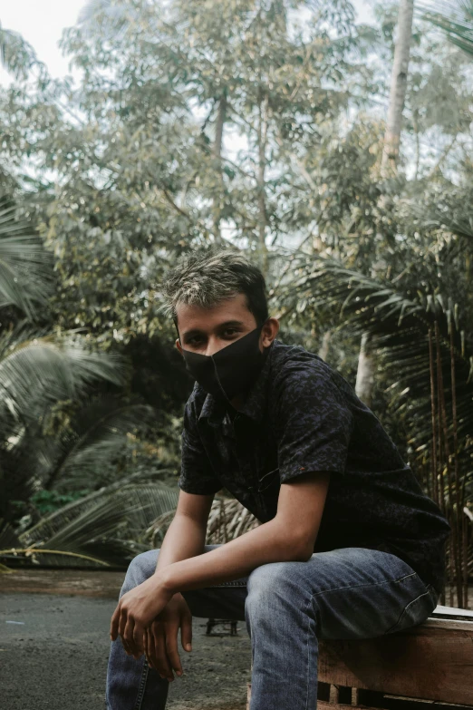 a man sitting on top of a wooden bench, an album cover, inspired by Erik Pevernagie, unsplash, sumatraism, wearing facemask, dark jungle, casual pose, low quality photo