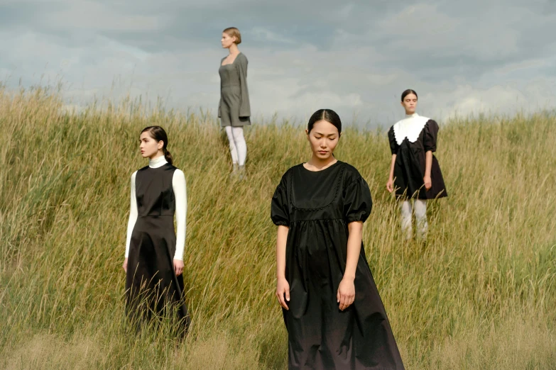 a group of people standing on top of a grass covered field, inspired by Vanessa Beecroft, hakama kimono, photograph of a techwear woman, uniform off - white sky, wearing a dark dress