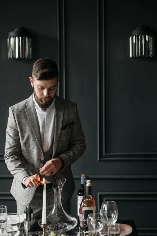 a man standing in front of a table with wine glasses, mixing drinks, grey suit, dark backdrop, thumbnail