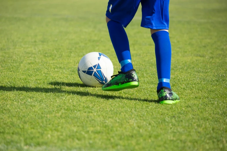 a person kicking a soccer ball on a field, a picture, green and blue, up close, clubs, profile pic