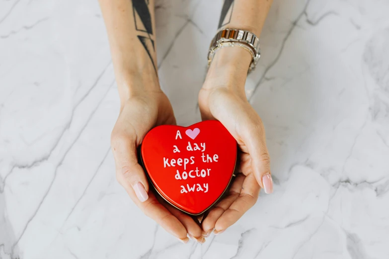 a woman holding a heart shaped box that says a day keeps the doctor away, a picture, pexels, metal lid, red, full product shot, back