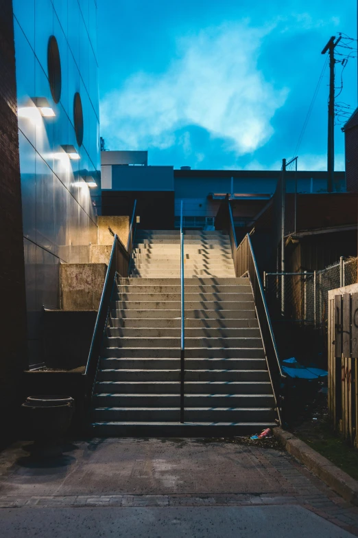 a set of stairs going up the side of a building, inspired by Elsa Bleda, unsplash contest winner, process art, evening at dusk, dramatic white and blue lighting, in an urban setting, industrial aesthetic