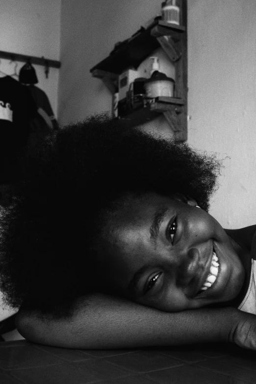 a little girl laying on top of a bed, a black and white photo, by Nadir Afonso, afrofuturism, detailed smile, long afro hair, 2 0 0 5, subject is smiling