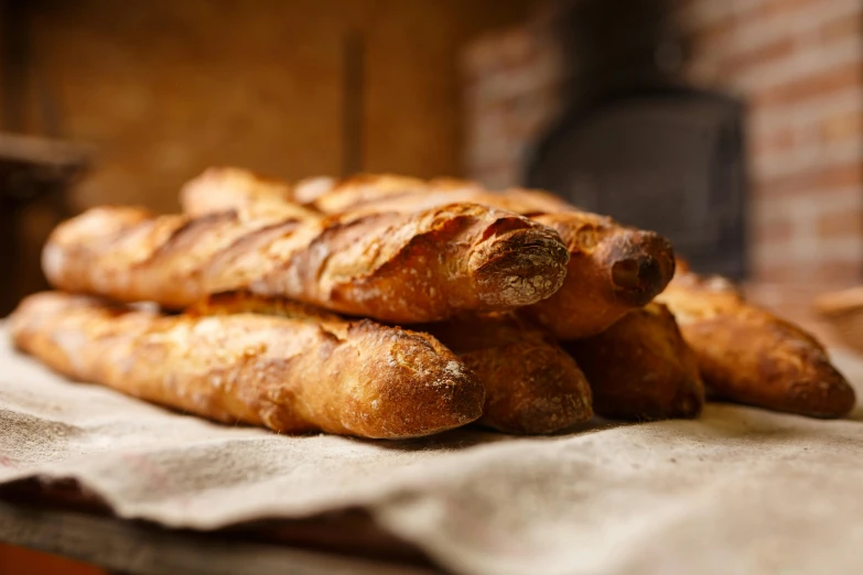 a pile of bread sitting on top of a table, inspired by Normand Baker, unsplash, figuration libre, baking french baguette, warmly lit, hot food, looking partly to the left