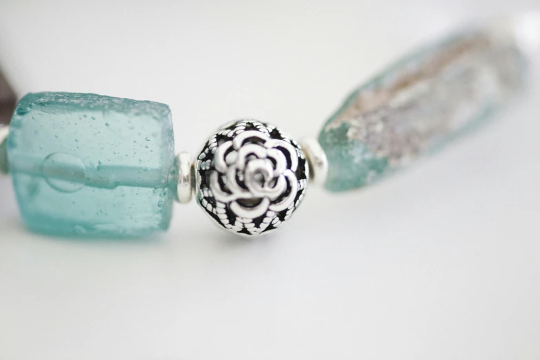 a couple of beads sitting on top of a table, inspired by Perle Fine, unsplash, arabesque, translucent roses ornate, aquamarine, detail shot, silver