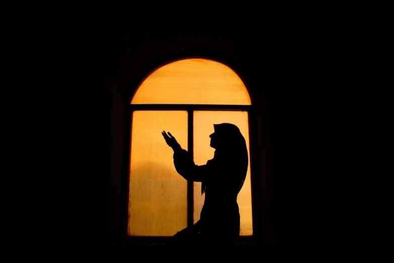 a silhouette of a woman standing in front of a window, inspired by Osman Hamdi Bey, pexels contest winner, hurufiyya, prayer hands, church window, phone photo, billie eilish as a nun