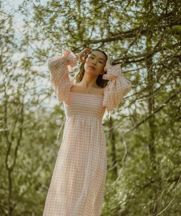 a woman standing in the woods wearing a pink checkered dress, an album cover, unsplash, happening, puff sleeves, mai anh tran, wearing a nightgown, on a sunny day