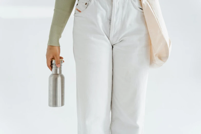a woman holding a water bottle and a bag, inspired by Sarah Lucas, trending on pexels, minimalism, white pants, stainless steel, recycled, small