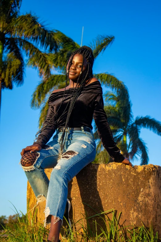 a woman sitting on a rock with palm trees in the background, an album cover, by Ingrida Kadaka, pexels contest winner, wearing jeans, black teenage girl, 15081959 21121991 01012000 4k, african queen