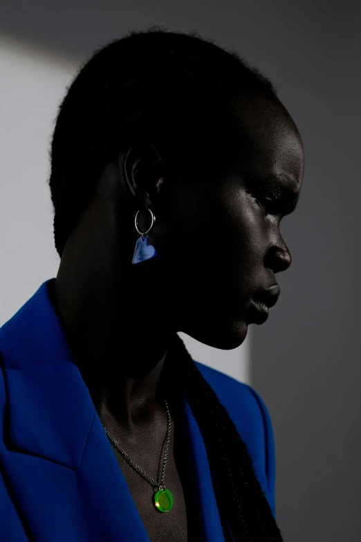 a woman in a blue jacket and green earrings, by artist, trending on unsplash, adut akech, photographed for reuters, cobalt blue, dark monochrome