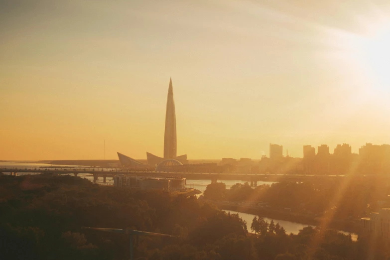 the sun is setting over the city skyline, by Andrei Kolkoutine, unsplash contest winner, modernism, obelisk, rostov, santiago calatrava, sunny amber morning light