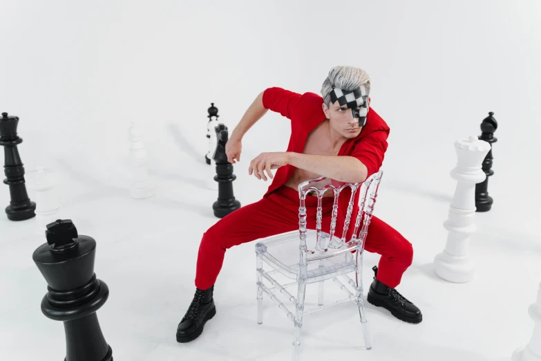 a man sitting on a chair surrounded by chess pieces, an album cover, inspired by Julian Allen, pexels contest winner, video art, red jumpsuit, crazy white hair, playful pose of a dancer, youtube thumbnail