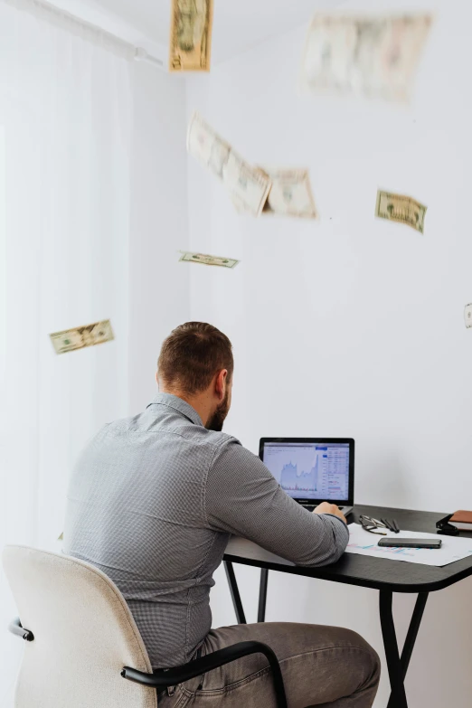 a man sitting at a desk in front of a laptop computer, by Julia Pishtar, pexels contest winner, dollar bills floating, minimalist home office, his back is turned, banner